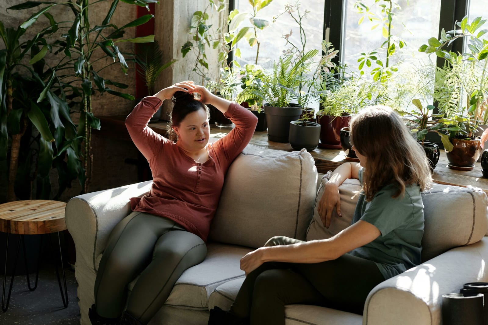 Deux amies en conversation sur un canapé, dans un salon rempli de plantes